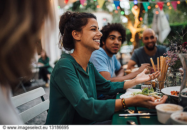 Smiling young women gesturing while sitting with friends at table during dinner party