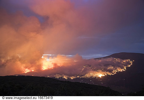 Smoke emitting from wildfire on mountain against sky at dusk
