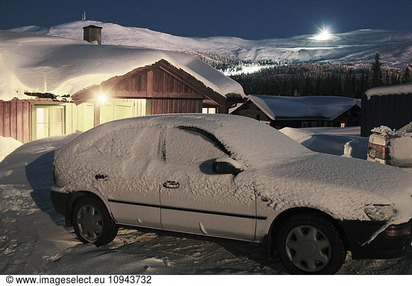 Snow covered car parked outside house at dusk