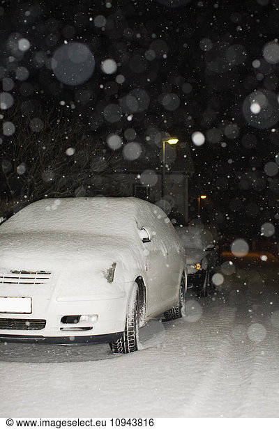 Snow covered cars parked on street at night