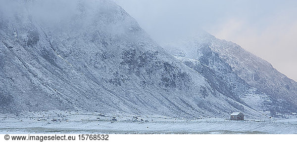 Snow covered mountain and remote cabin Flakstad Lofoten Norway