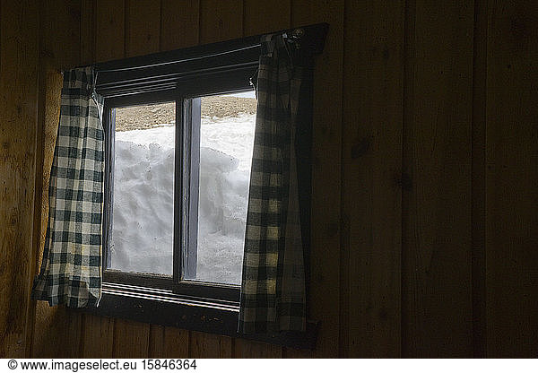 Snow packed against a wood cabin window as seen from the inside