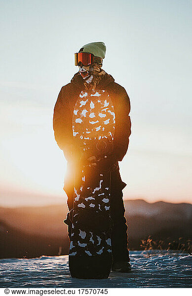Snowboarder in sportswear and snowboard on the mountain at sunset