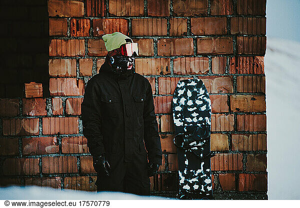 Snowboarder posing wearing snowsuit close to a brick wall