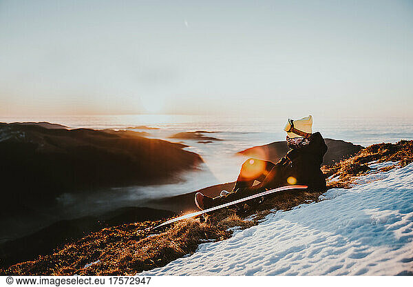 Snowboarder relaxing at sunrise on the mountain above clouds
