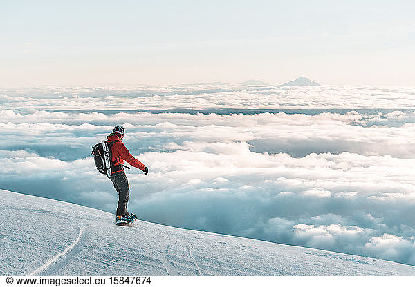 Snowboarder riding down mountain at sunset above clouds