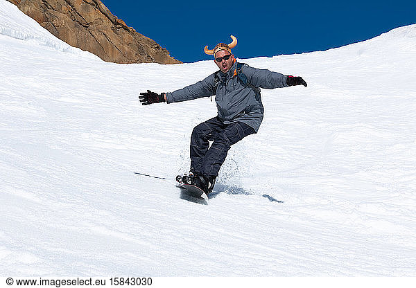 Snowboarder running down the slope in ski resort with a funny hat.