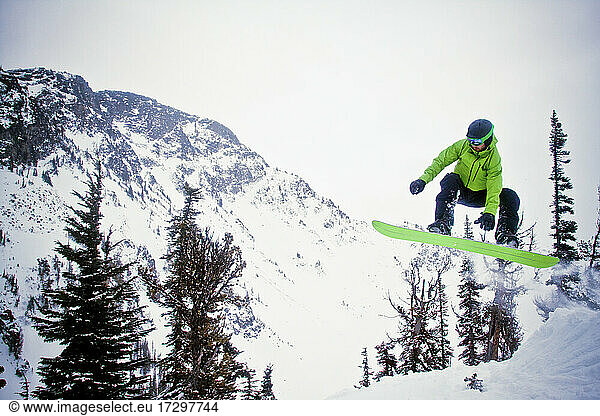 Snowboarder wearing green in mid-air after launching off snow jump.