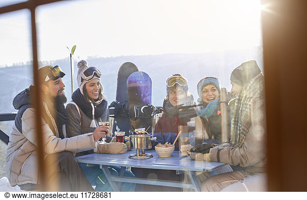 Snowboarderfreunde beim Trinken und Essen am Balkontisch Apres-Ski