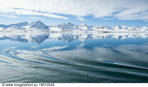 Snowy mountains reflecting in the sea  in the foreground a boat wake
