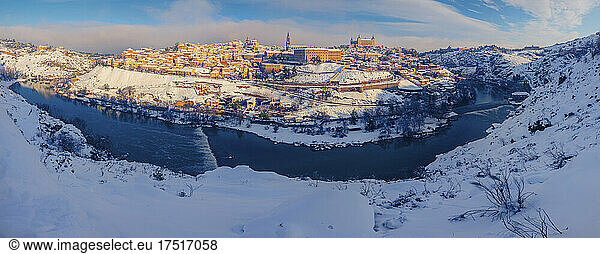 Snowy old town with castle on river hill with golden colors at sunset