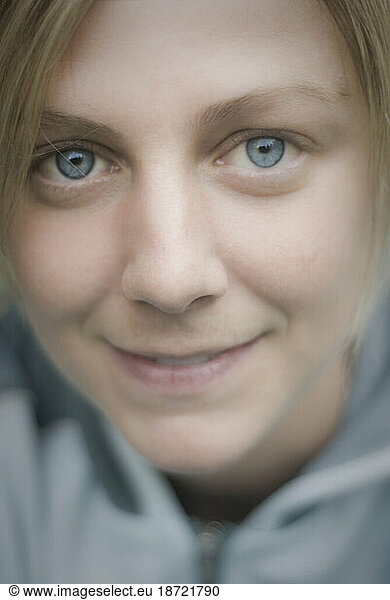 Soft close up portrait of a content young woman with blue eyes wearing a blue fleece jacket.