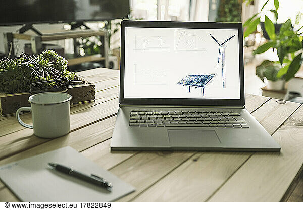 Solar panel and wind turbine on screen of laptop at home