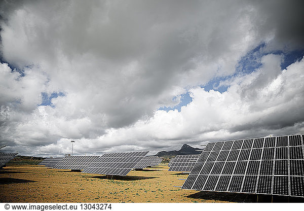 Solar panels on landscape against cloudy sky