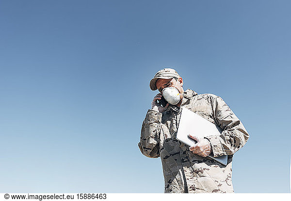 Soldat mit Gesichtsmaske bei Notfalleinsätzen  mit Smartphone  mit Laptop