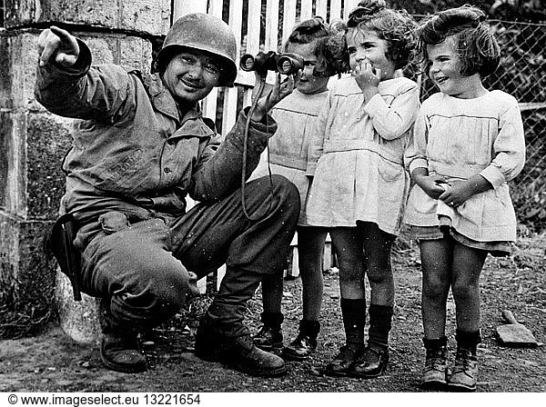 Soldier holding binoculars up to three little girls.