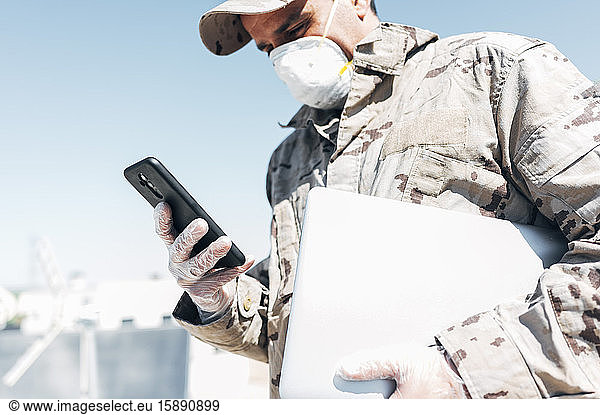 Soldier with face mask on emergency operation  using smartphone  carrying laptop