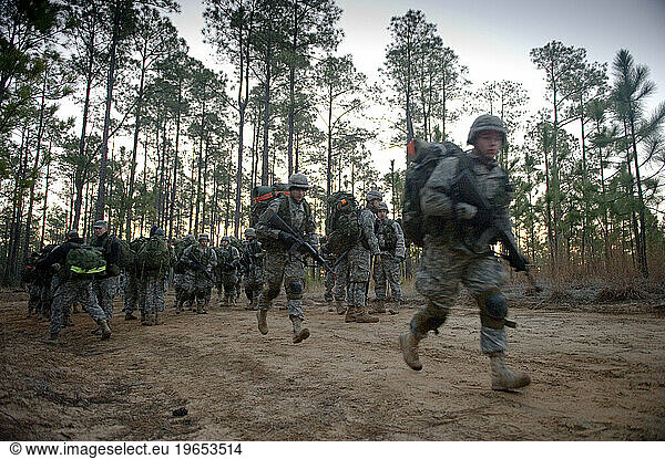 Soldiers run down a dirt road with their rucks and weapons during a field training exercise.