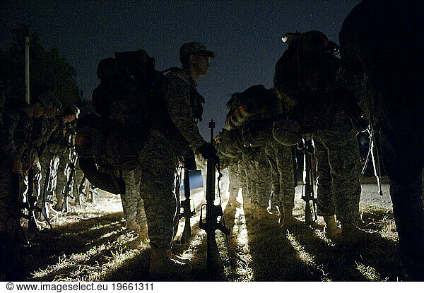 Soldiers stand in formation near a dirt road in the middle of the night during a field training exercise.