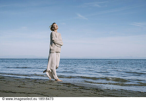 Solitude woman with arms crossed walking on shore at beach