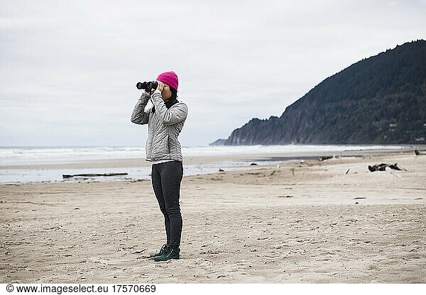 Solo Woman looking through binoculars alone on Oregon beach