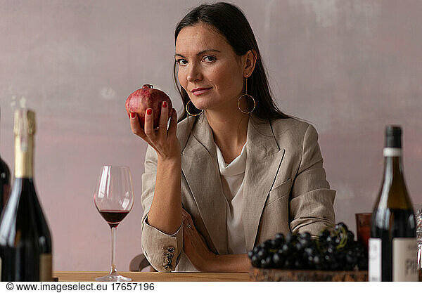 Sommelier woman among wine bottles holding pomegranate fruit