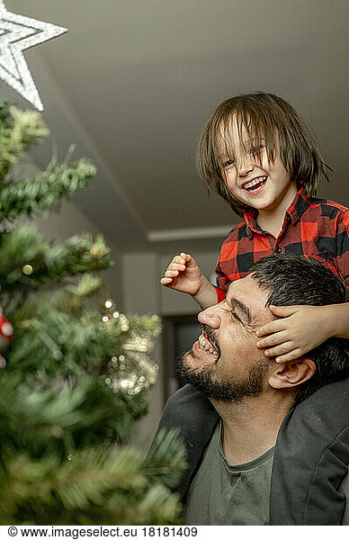 Son and father having fun by Christmas tree at home