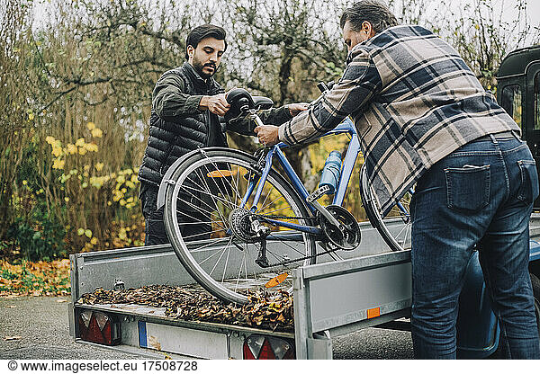 Son and father loading bicycle in vehicle trailer on driveway