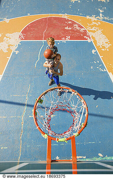 Son and father playing basketball at sports court
