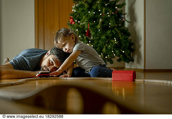 Son and father playing with toy train in front of Christmas tree