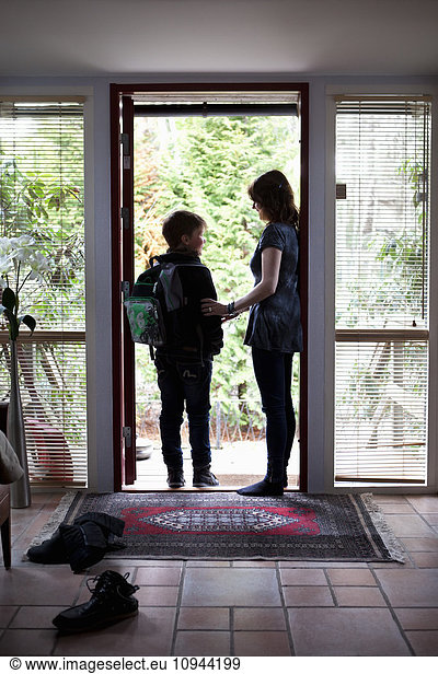 Son carrying book bag standing with mother at door