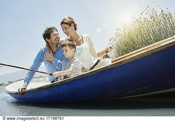 Son fishing while sitting by parents in rowboat during sunny day