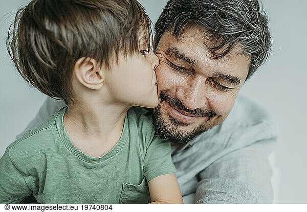 Son kissing father on cheek against white background