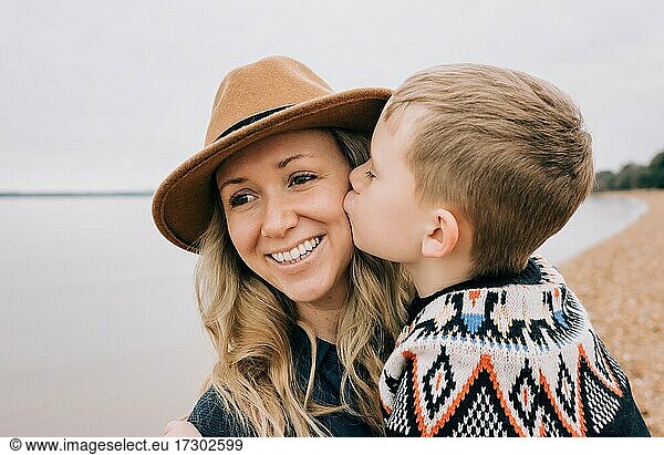 son kissing his moms cheek whilst at the beach happily playing