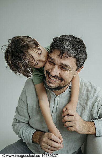 Son kissing smiling father against white background