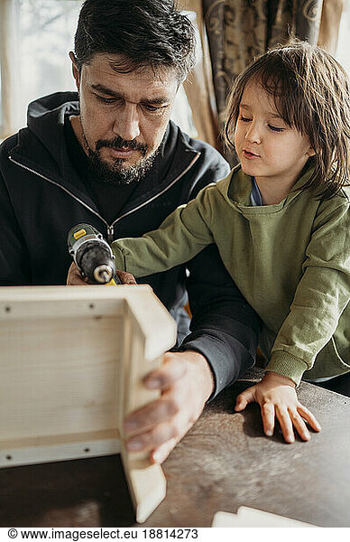 Son learning to build up birdhouse with father at home