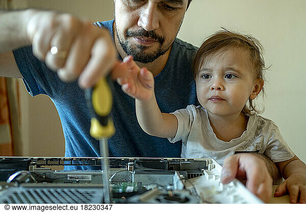 Son looking at father repairing computer at home