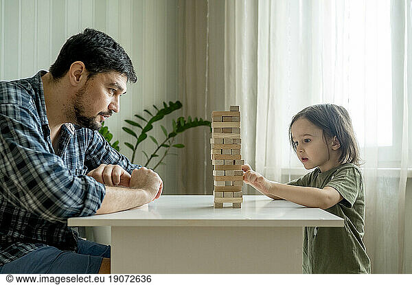Son playing jenga with father on table at home