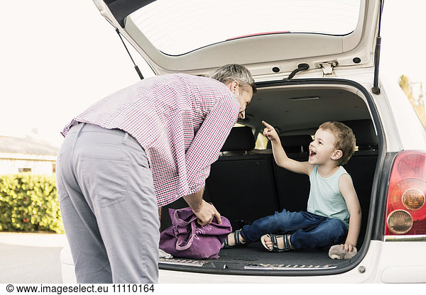 Son pointing at father while sitting in open car trunk