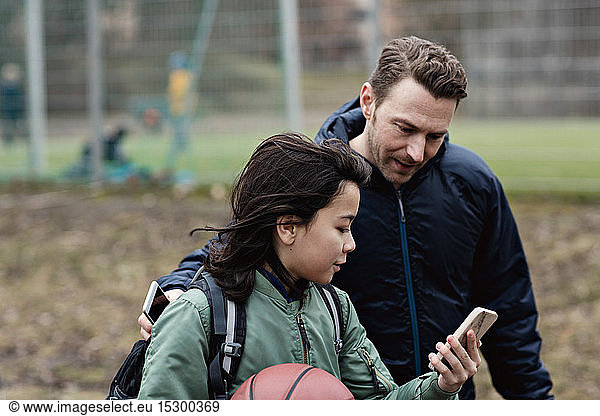 Son showing his smart phone to father while standing by sports court