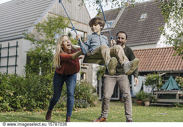Son swinging in garden with parents pushing him