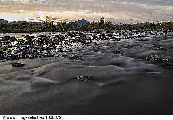 Sonnenuntergang über dem fließenden Wasser des Flusses Tsielekjåhkå  vorbei am Kungsleden Trail  Lappland  Schweden