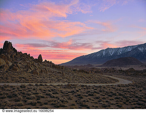 Sonnenuntergang hinter Felsformationen in einer trockenen Wüstenlandschaft.