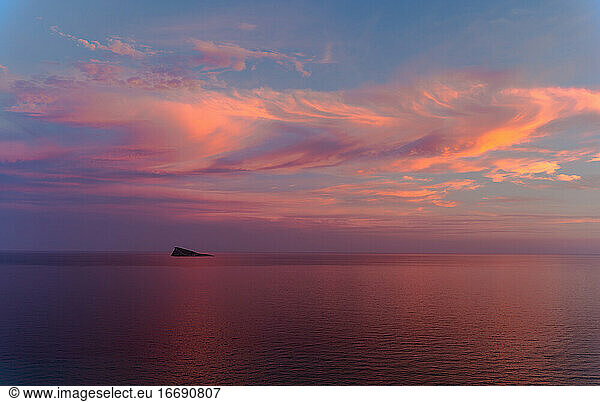 Sonnenuntergang in Benidorm / Valencia / Spanien mit einem bewölkten blauen und orangenen Himmel und einer Insel am Horizont des Mittelmeers mit einer orangen  roten  blauen und rosa Farbe. Horizontal Foto