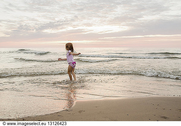 Sorgloses Mädchen spielt am Strand am Strand gegen bewölkten Himmel bei Sonnenuntergang