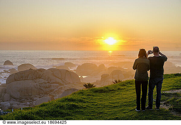 South Africa  Western Cape Province  Cape Town  Tourists photographing Atlantic Ocean at sunset
