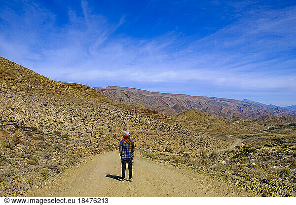 South Africa  Western Cape Province  Male hiker standing in middle of empty dirt road in Great Karoo