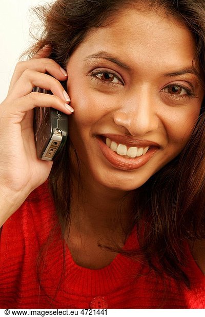 South Asian Indian teenager girl using red contact lenses in eyes and brown hair very joyfully talking on mobile phone MR686G