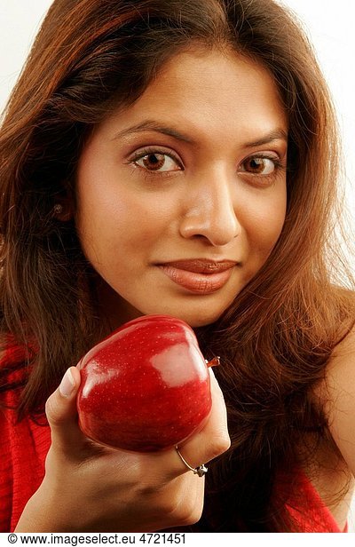 South Asian Indian teenager girl wearing red colour contact lenses in eyes and brown hair showing fresh red apple as fruit good for health MR686G