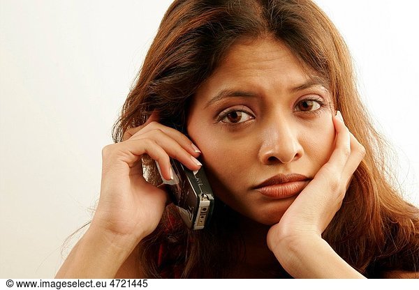 South Asian Indian teenager girl wearing red colour contact lenses in eyes disappointingly talking on mobile phone MR686G